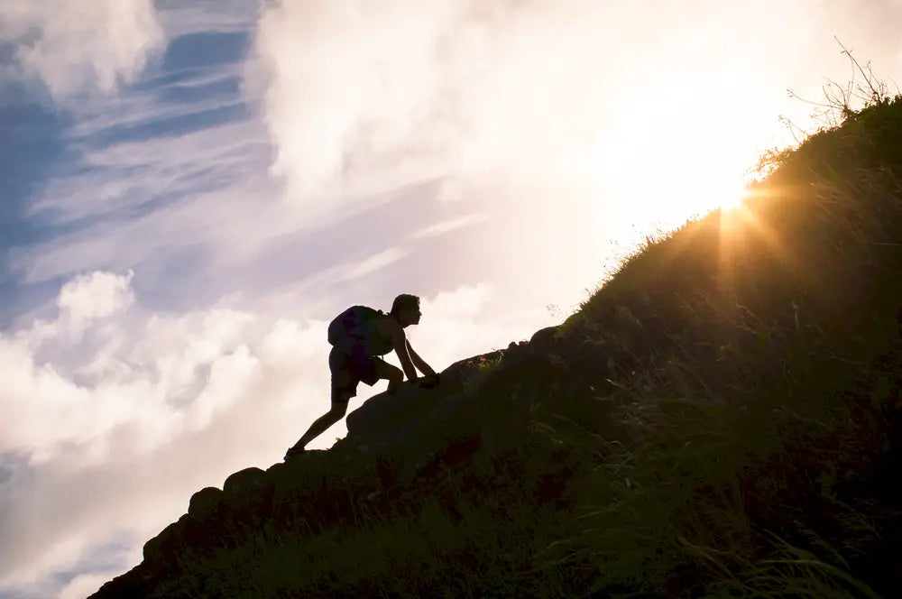 Man climbs up a hill at sunrise depicting the concept of endurance